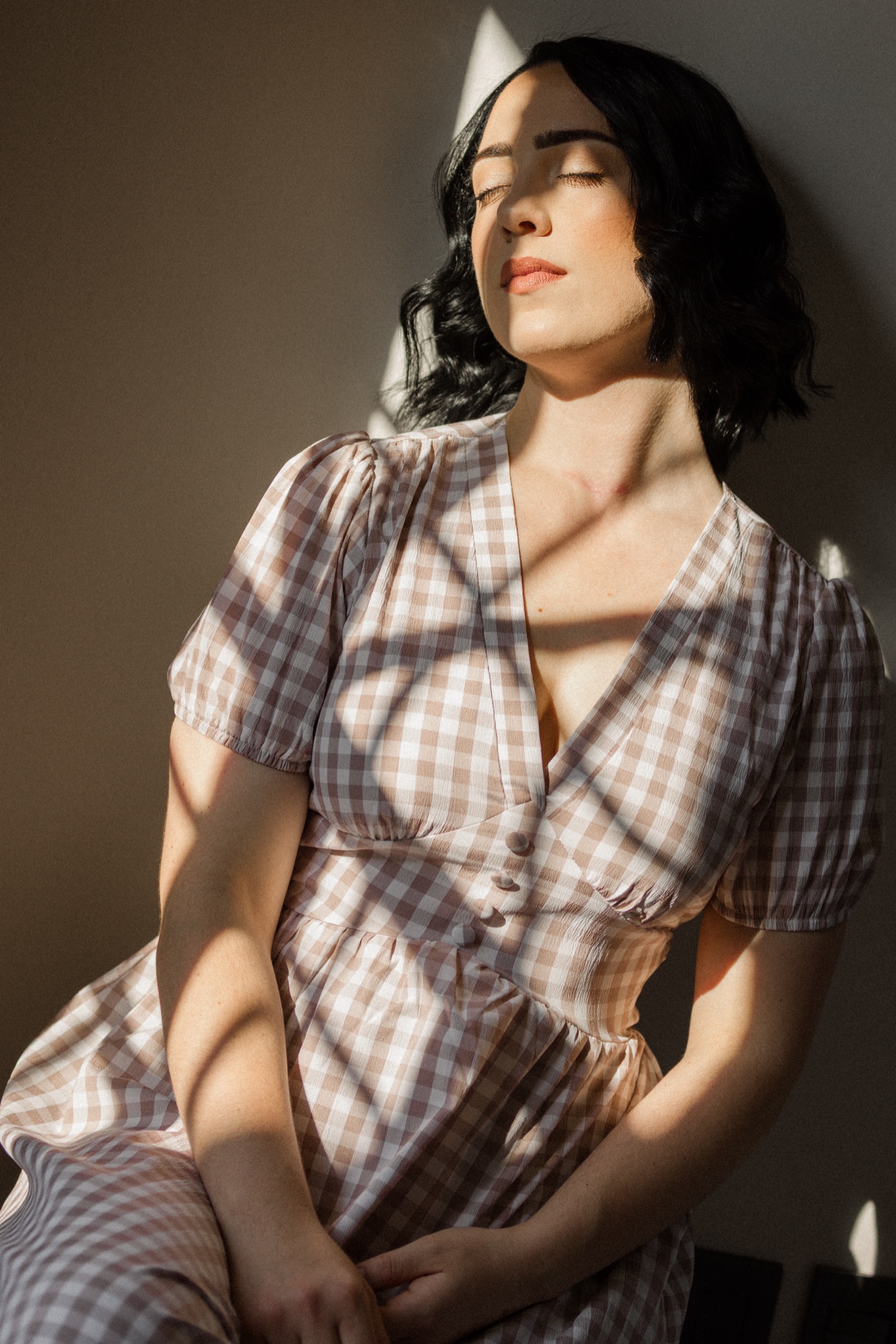Simone in a pink and beige gingham dress, eyes closed in warm window light.
